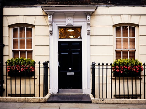 Beautiful curb appeal of a house with seashell colored exterior walls, white windows and trim around the black door and a black iron fence.