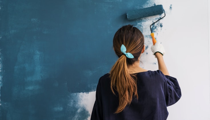 Woman painting interior wall with paint roller in new house