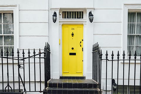 Beautiful curb appeal of a house with white colored exterior walls, black iron fence, lamps, door knobs, and a yellow front door.