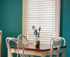 Minimalistic kitchen with teal colored walls, white window, white chairs and a wooden table.