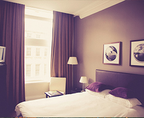 A hotel room painting project. The walls have been painted purple, matching purple curtains hang on the window, creating a nice contrast to the white bed sheets.