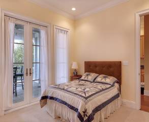 Pastel yellow painted bedroom with a large double bed in the middle and white vintage doors, leading to a terrace.