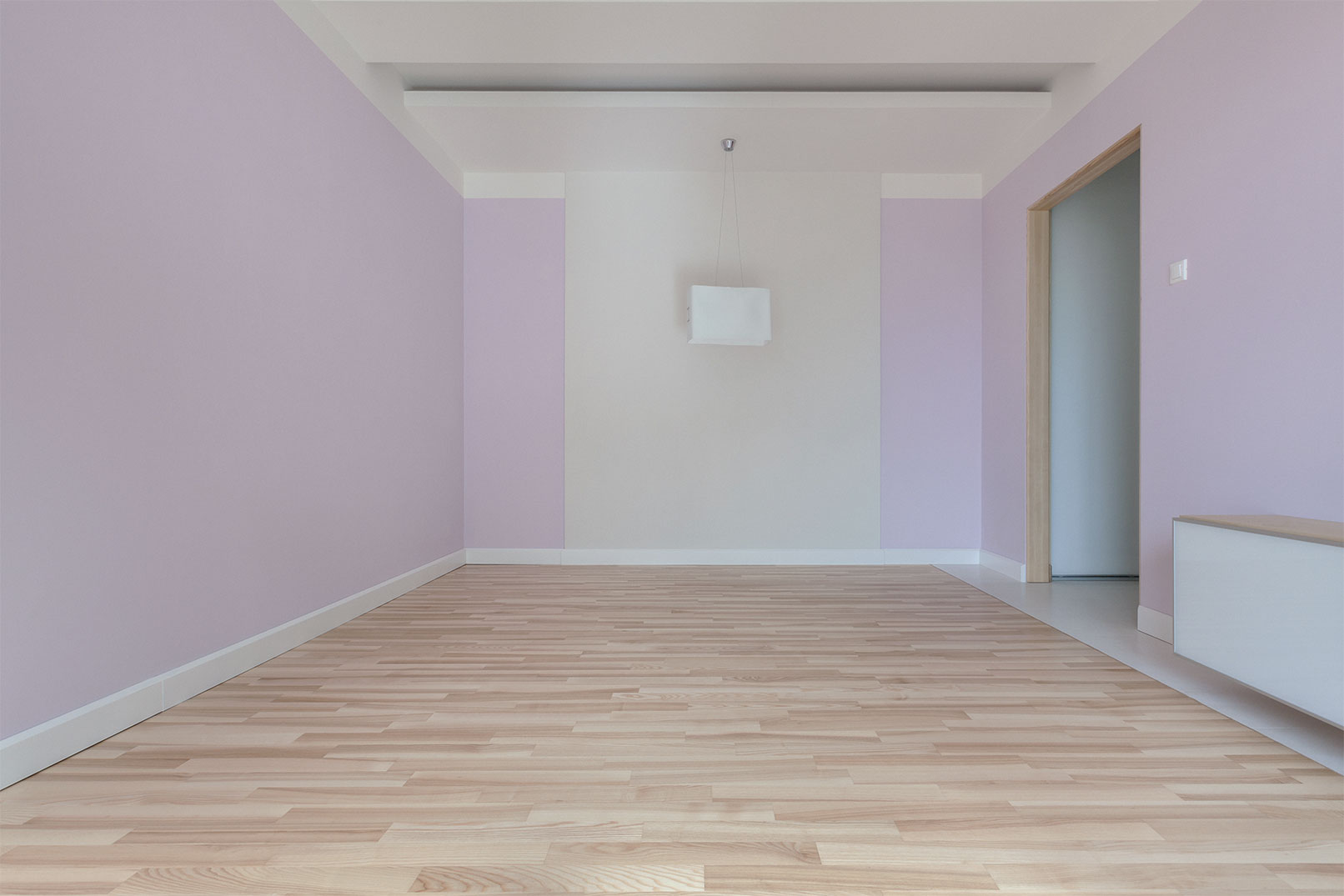 Pastel pink colored room with white trim, seashell colored ceiling and light wooden floor.