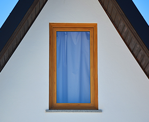 Closeup of a white townhouse exterior with a big window that’s covered with blue curtains.