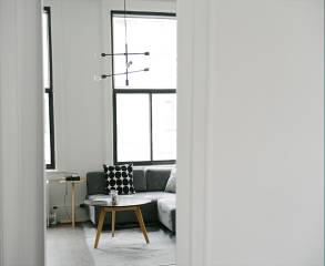 White interior of loft in Chicago, with large dark framed windows, grey couch and a coffee table in the center of the room.