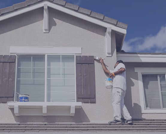 A painter is standing on a rooftop and painting the exterior of a house.