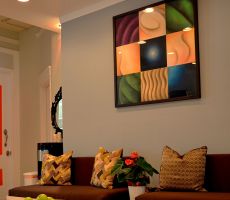 Grey living room with brown furniture, modernist painting on the center of the wall and a white door with bright orange stripes.