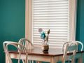 Minimalistic kitchen with teal colored walls, white window, white chairs and a wooden table.