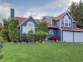 A house with blue exterior paint, bright red roof, large white windows and tidy landscaping.