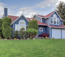 A house with blue exterior paint, bright red roof, large white windows and tidy landscaping.