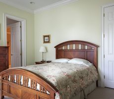 Light green bedroom with dark colored wooden furniture, white doors, two paintings hanging on the walls and white doors. 