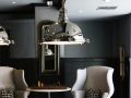 Luxury interior with two grey armchairs, a table with a chess board, large metal lamps and and a modern mirror hung on a half grey and half black painted wall.