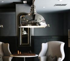 Luxury interior with two grey armchairs, a table with a chess board, large metal lamps and and a modern mirror hung on a half grey and half black painted wall.