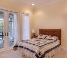 Pastel yellow painted bedroom with a large double bed in the middle and white vintage doors, leading to a terrace.