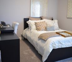 Small bedroom with a black, decorated twin bed, black desk with white and gold colored decorations on top and a white chair next to it, gray carpet and gray painted walls. 