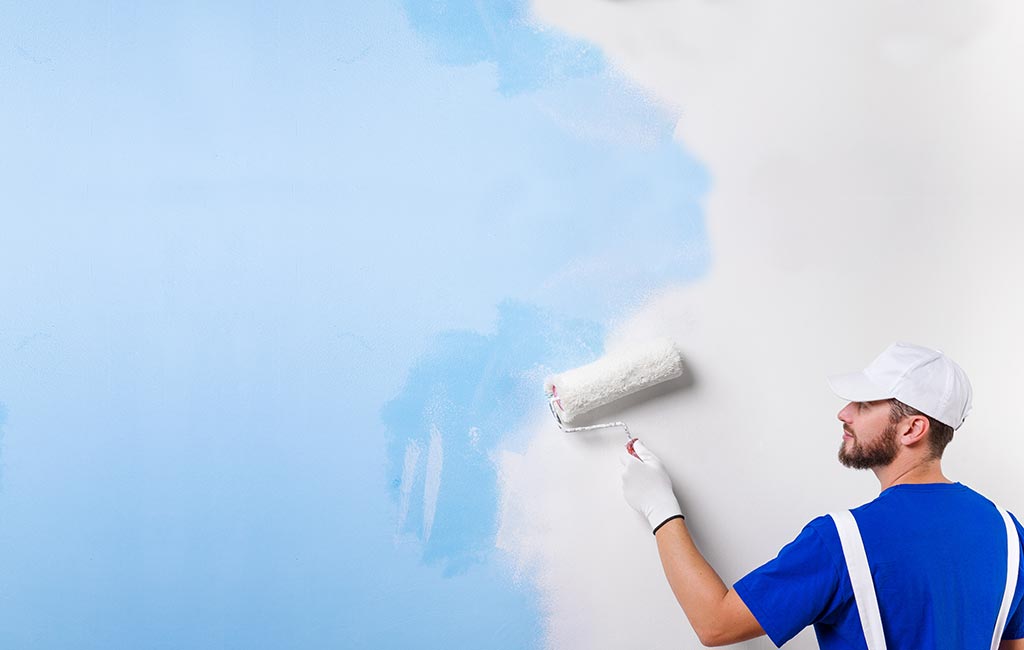 A painter is painting over a blue wall with white paint.